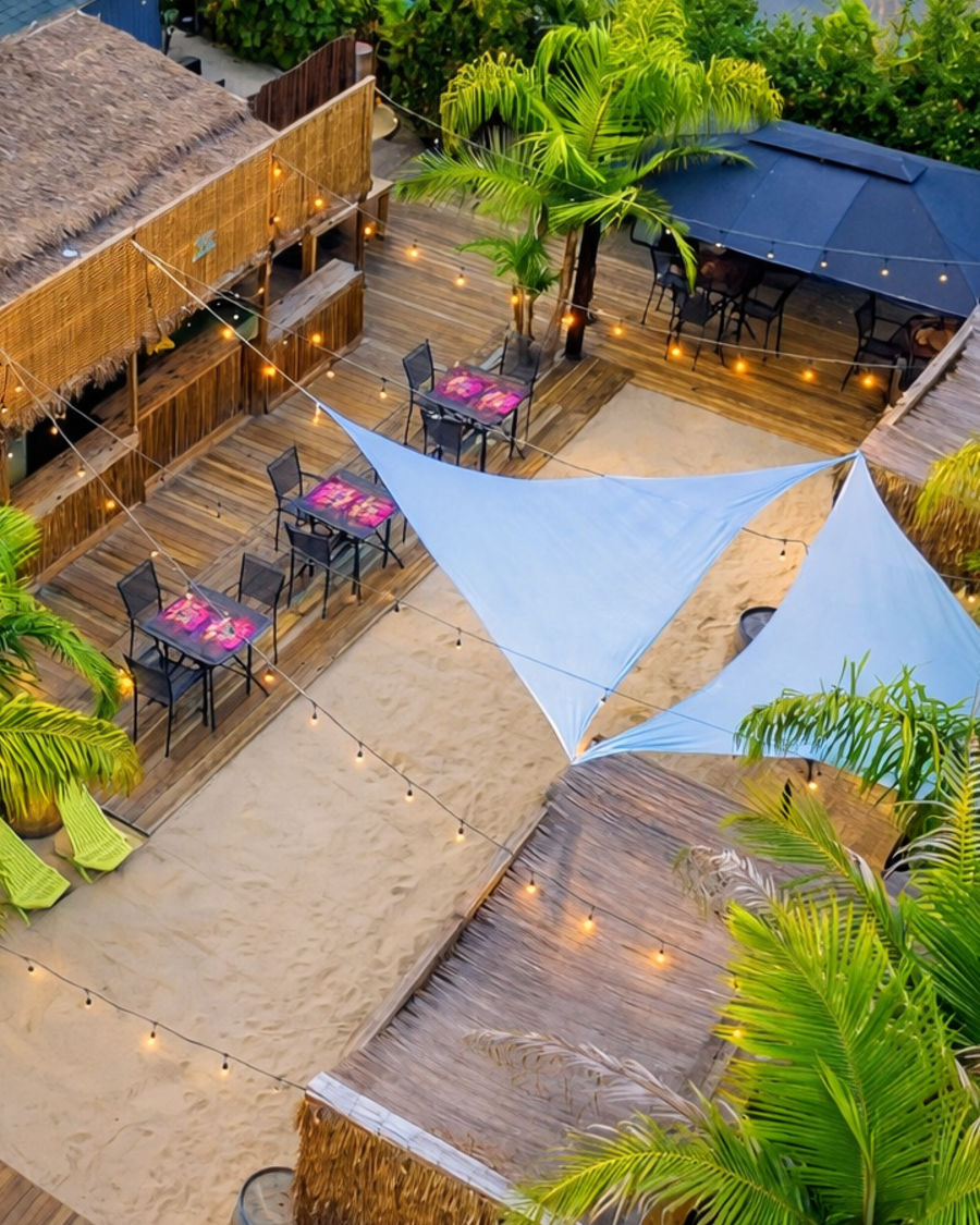 Aerial view of Good Life Resort — sand patio with sail shades, palms, tiki bar, and string lights